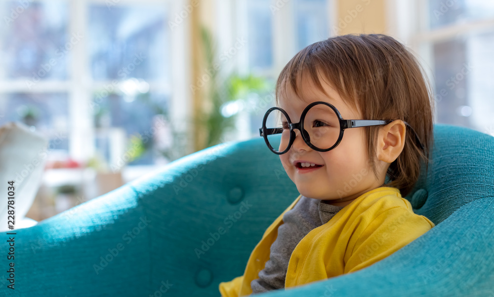 Happy toddler boy with glasses playing in a big chair