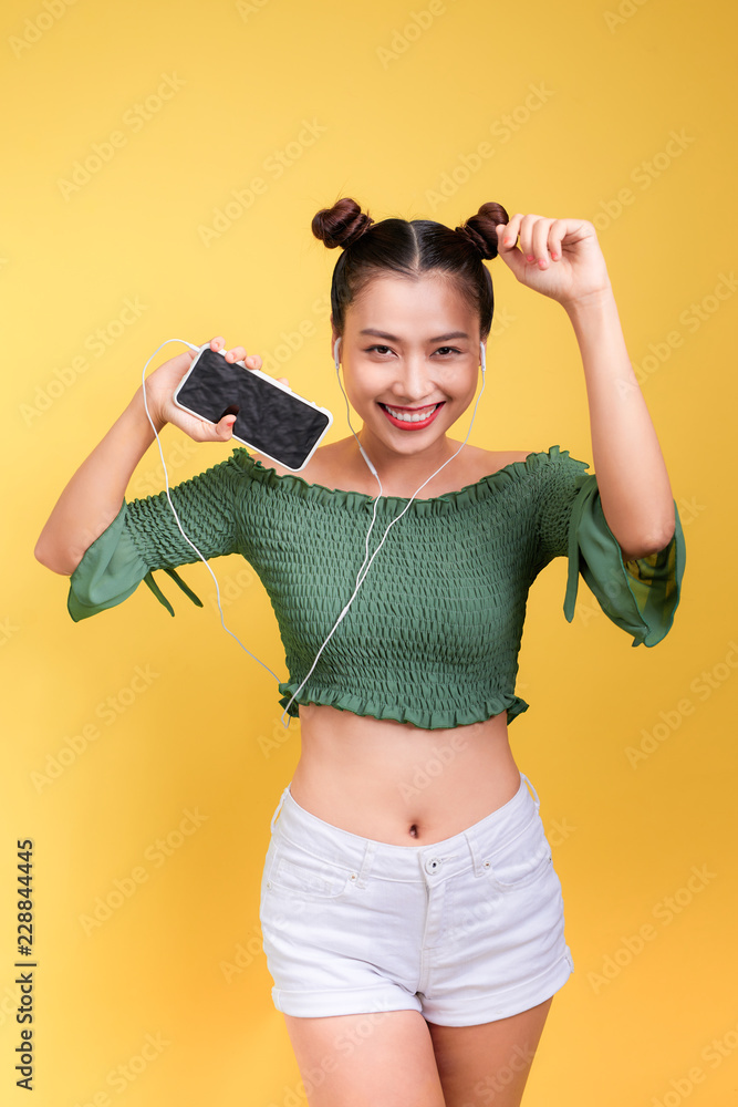 时尚微笑的亚洲女人戴着黄色背景的耳机听音乐