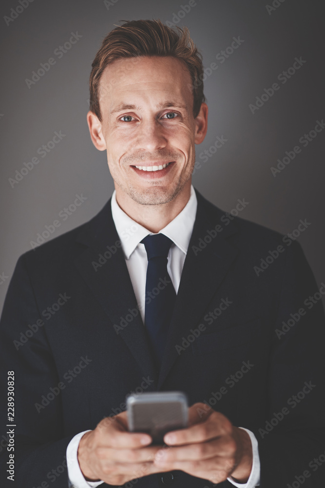 Smiling young business executive sending texts against a gray ba