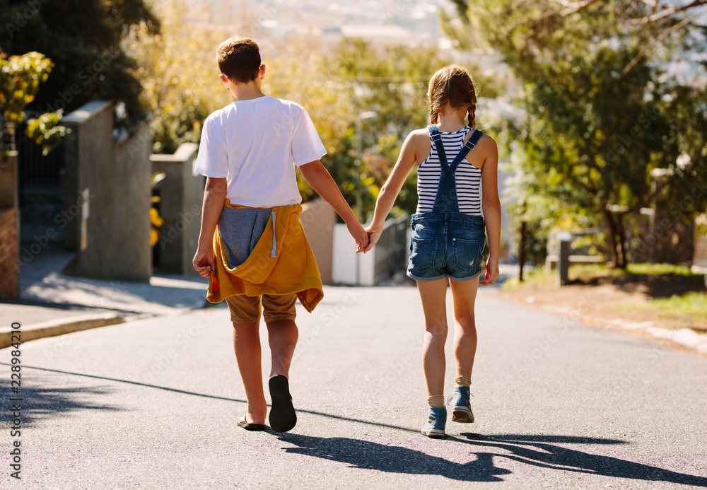 Rear view of kids walking on road holding hands