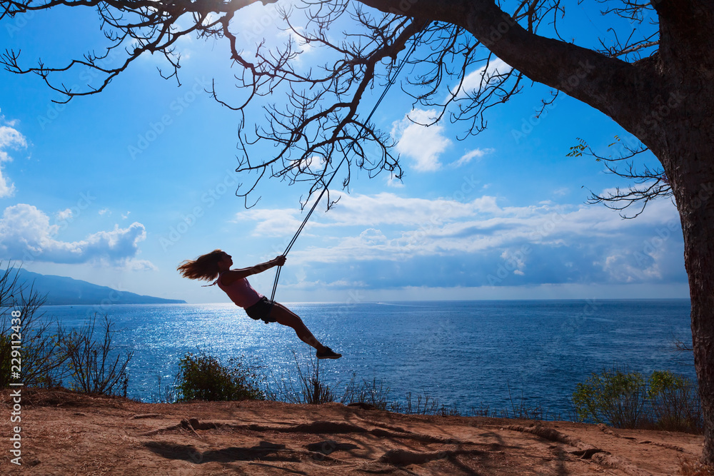 Happy girl have fun swinging high in mid air. Flying up upside down on rope swing on sea beach. Trav