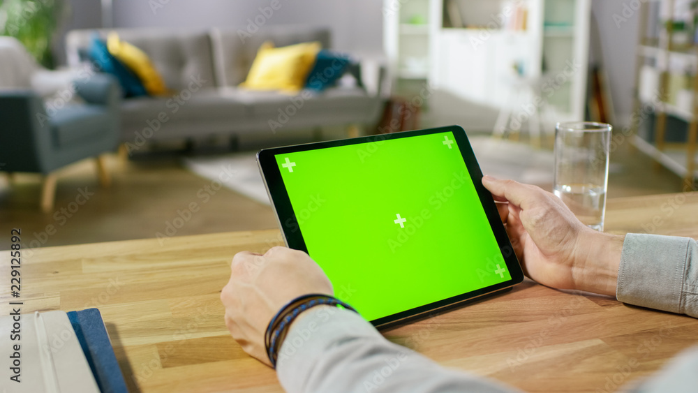 Man Holding Green Mock-up Screen Digital Tablet Computer While Sitting at the Desk. Man Buying stuff