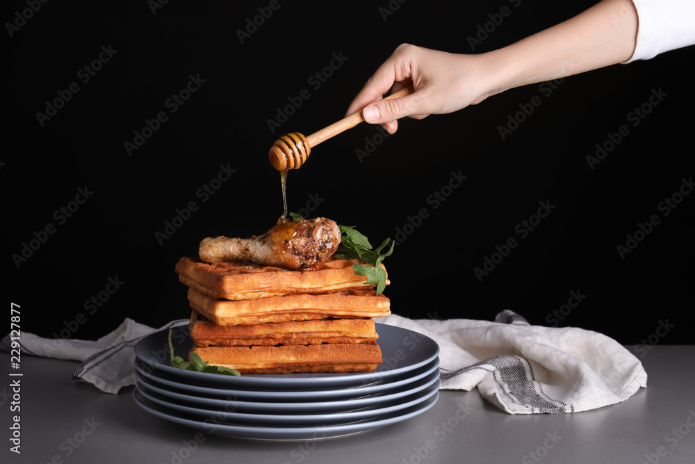 女人在深色背景下倒鸡腿和蜂蜜华夫饼