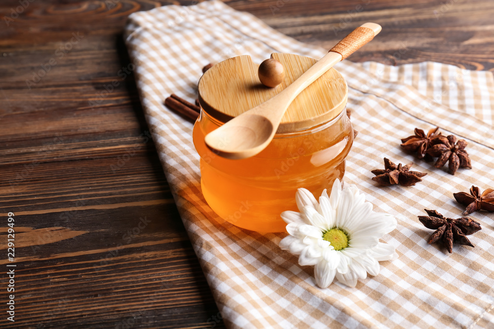 Jar with honey, spoon and spices on wooden table