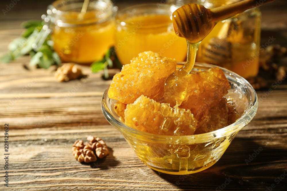 Dipper and bowl with sweet honeycomb on wooden table, closeup