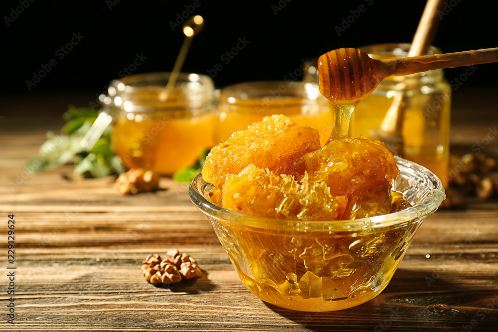 Dipper and bowl with sweet honeycomb on wooden table against dark background