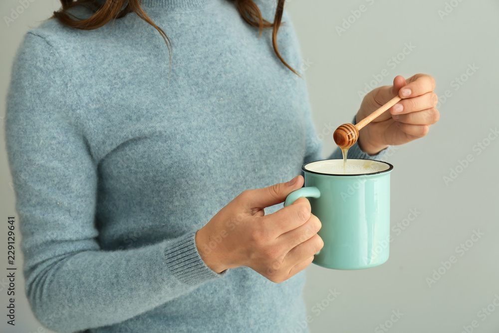 女人在灰色背景的牛奶杯中加入蜂蜜，特写