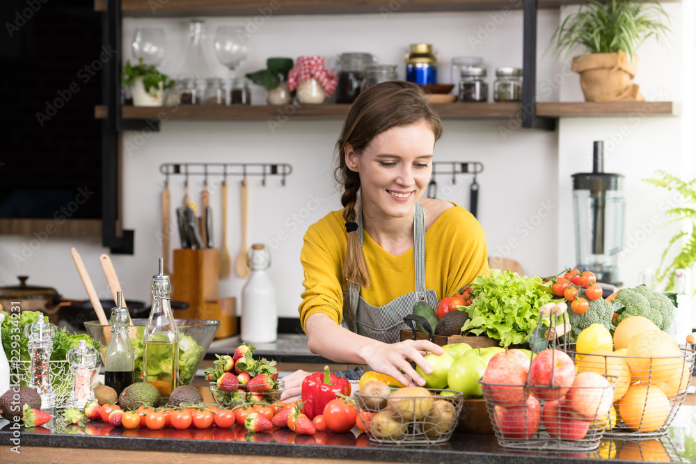 Healthy young woman in a kitchen preparing fruits and vegetables for healthy meal and salad