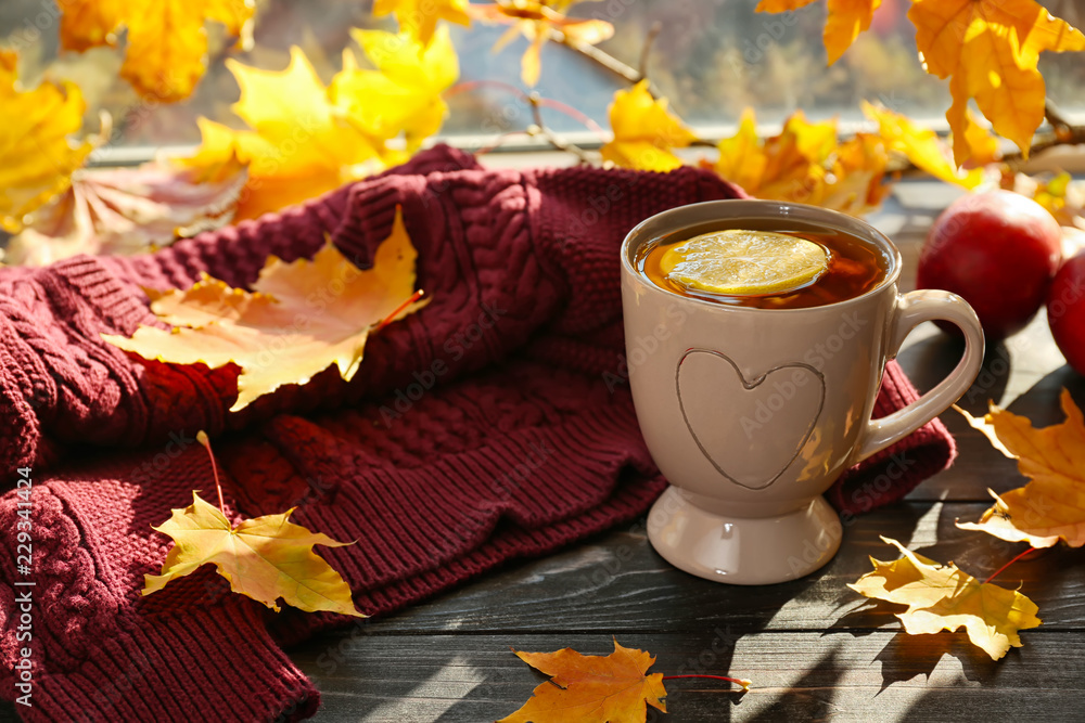 Cup of aromatic tea with autumn leaves on windowsill