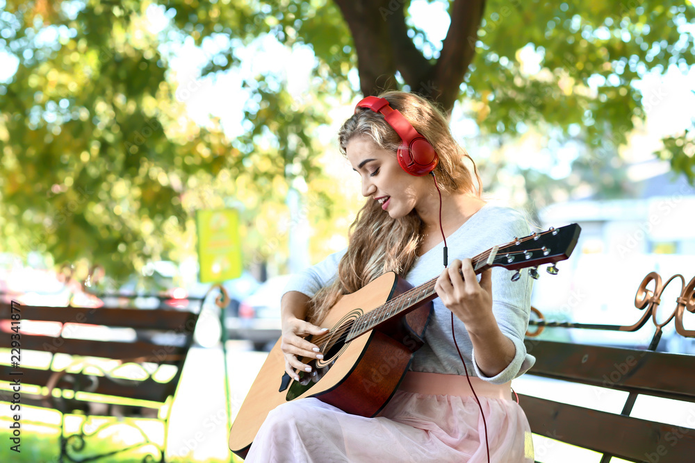 Beautiful young woman listening to music and playing guitar in park