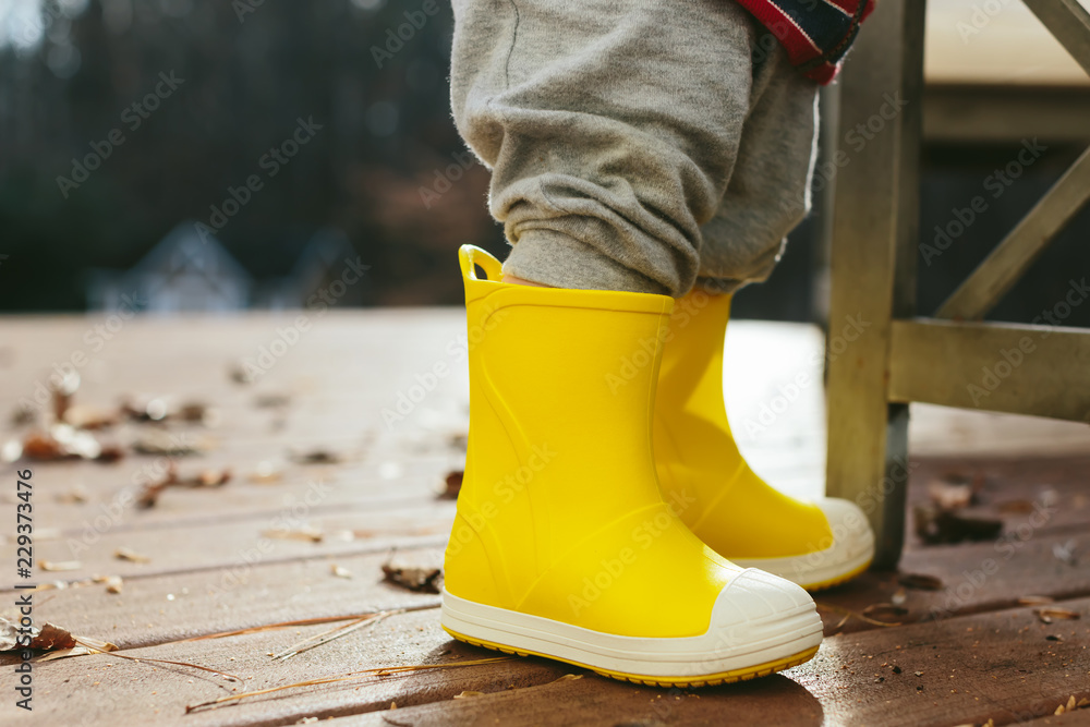 Toddler boy playing with his yelllow rain boots in autumn