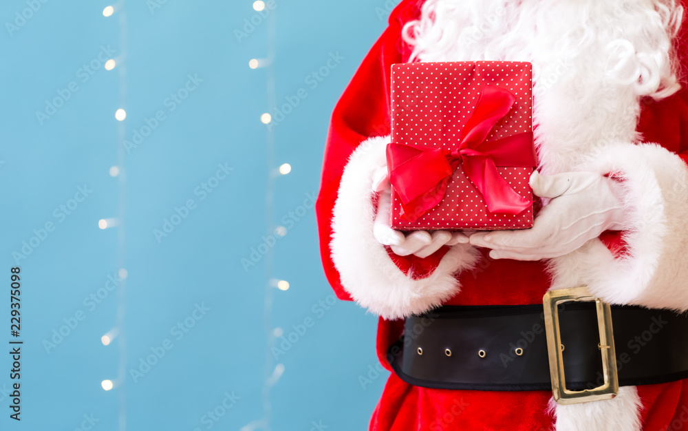 Santa holding a Christmas gift on a shiny light blue background