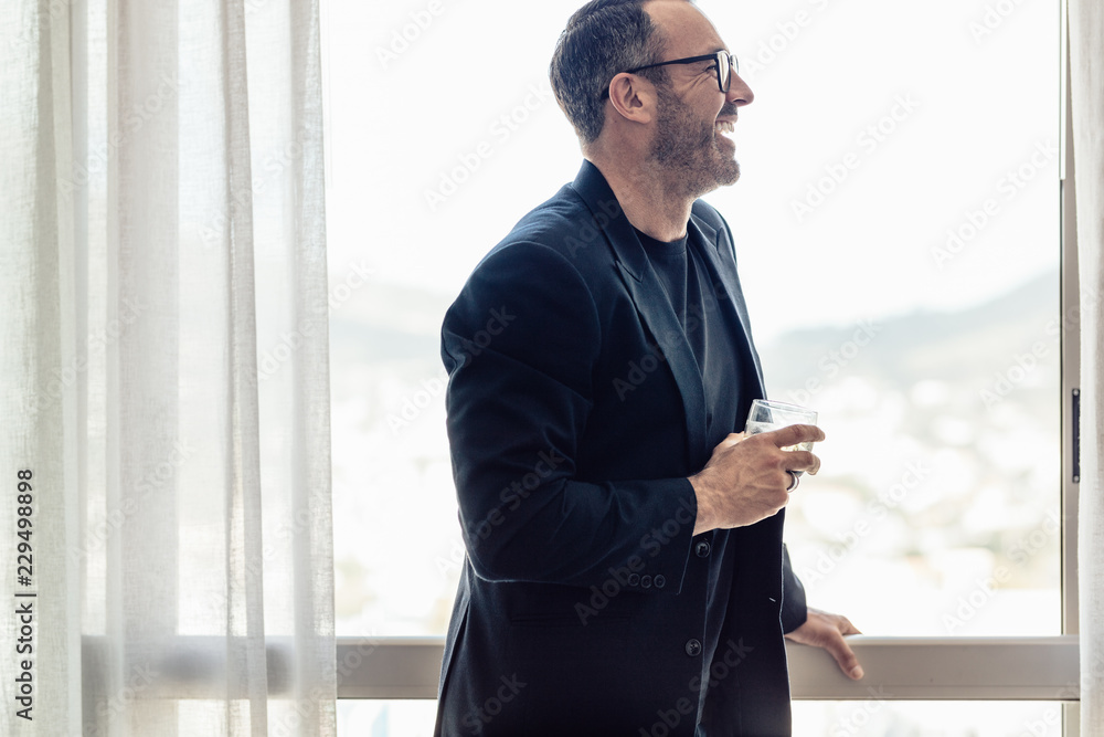 Mid adult businessman with glass of drink in hotel room