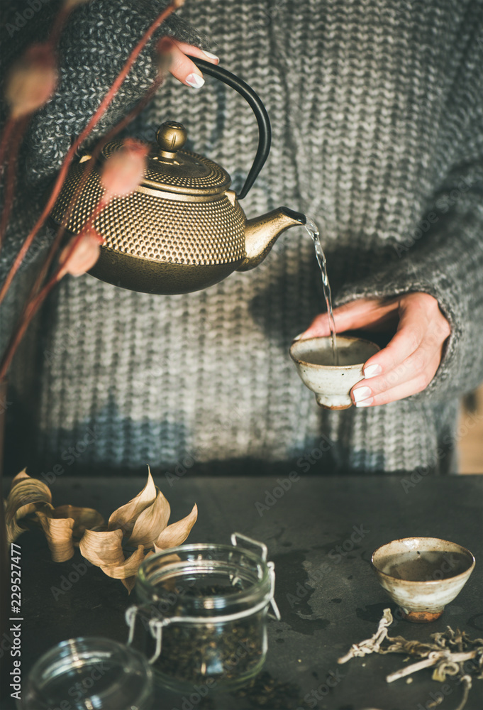 茶道。穿着灰色保暖针织冬衣的女人从金色的铁茶壶里倒绿茶