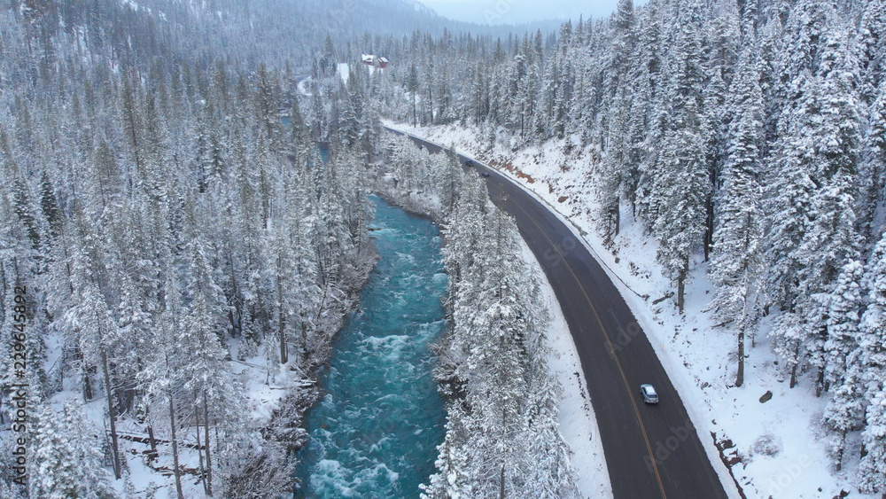 空中飞航：旅游车在白雪皑皑的树林和翡翠河中巡游。