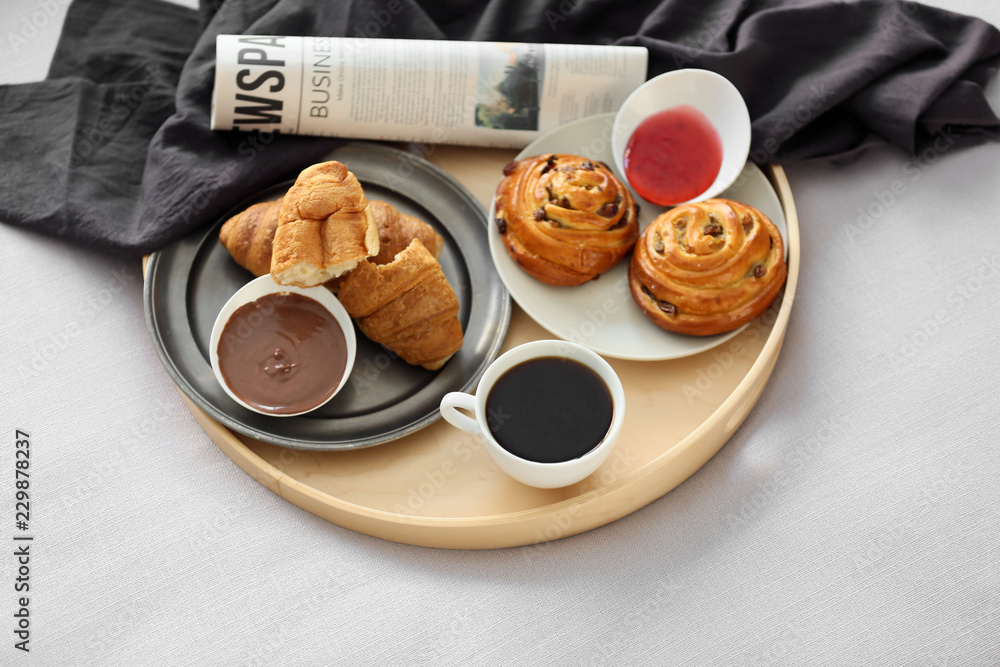 Tray with delicious breakfast and newspaper on bed