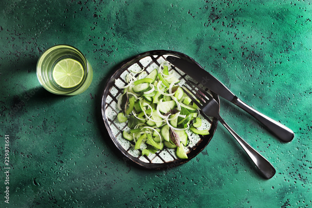 Plate with healthy vegetable salad and glass of water on color table