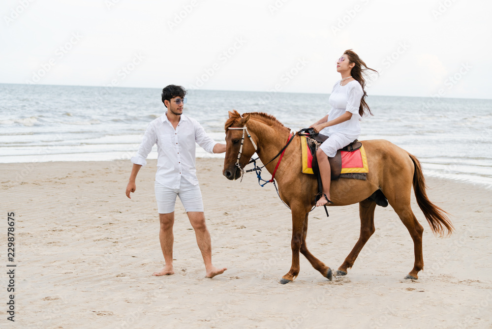 Young couple goes horse riding on tropical beach.