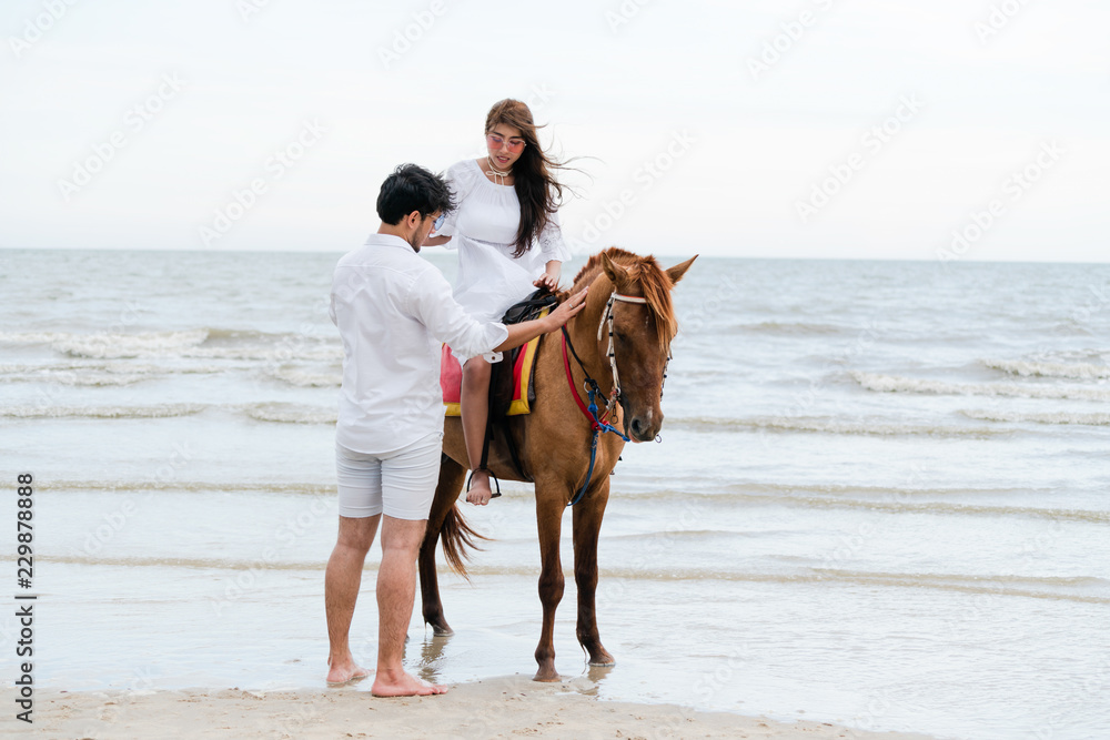 Young couple goes horse riding on tropical beach.