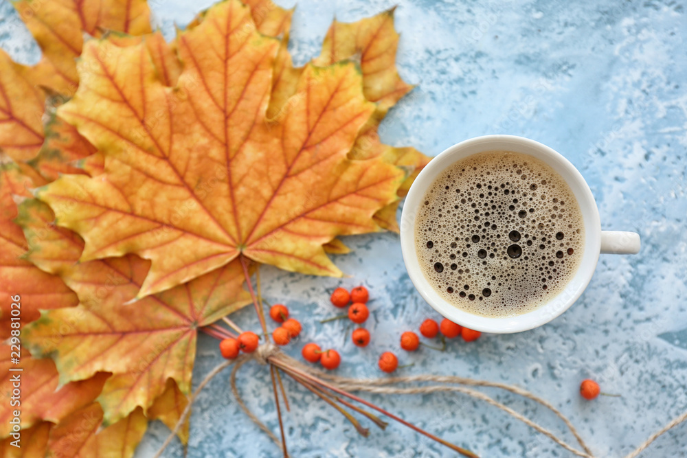 Cup of hot coffee with autumn leaves on color table