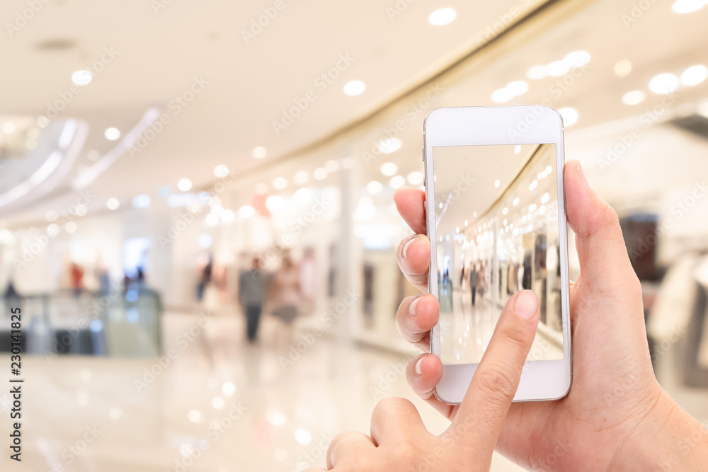 Woman hands Taking a picture with a smart phone in shopping mall with blurred image of clothes shop.