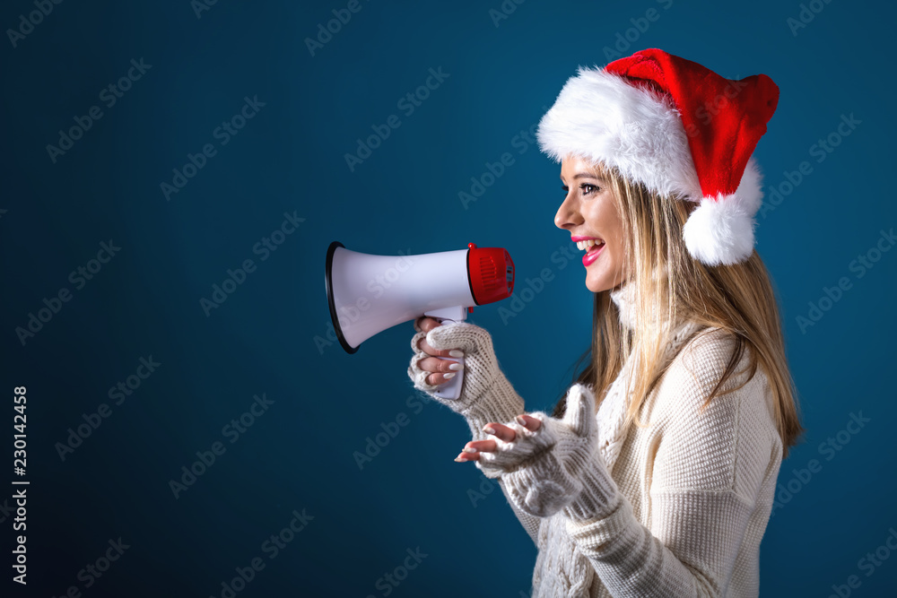 Young woman with santa hat holding a megaphone on a dark blue background