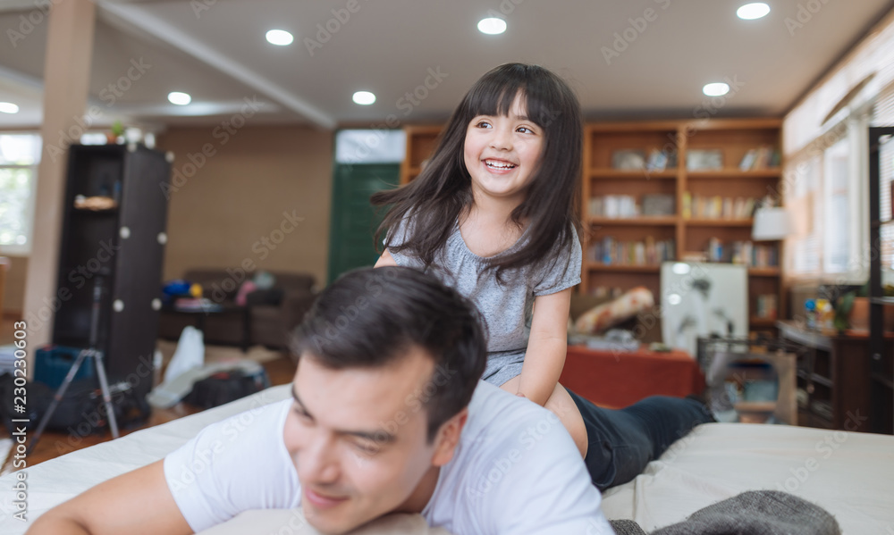 快乐的小女孩女儿和爸爸一起玩，骑爸爸回来，爸爸躺在家里的床上