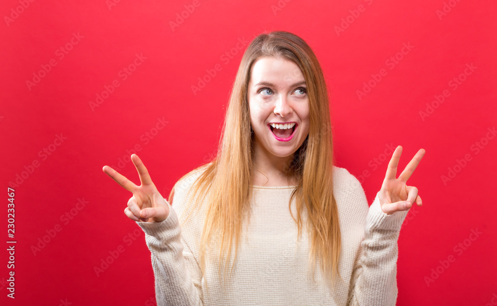 Young woman giving the peace sign on a solid background