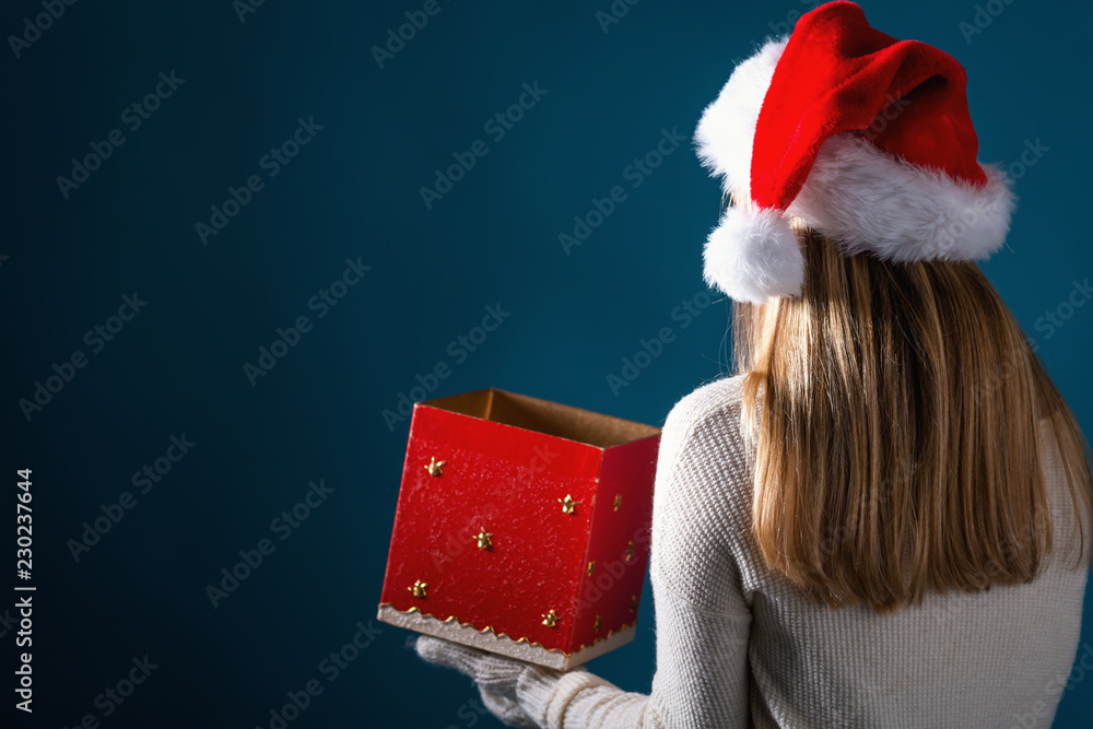 Young woman with santa hat opening a Christmas gift box on a dark blue background