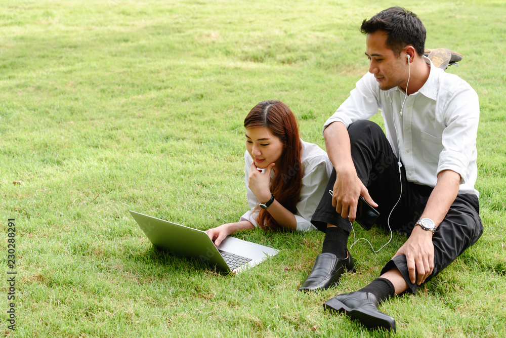 Man and woman in white shirt use smartphone and laptop together in outdoors park