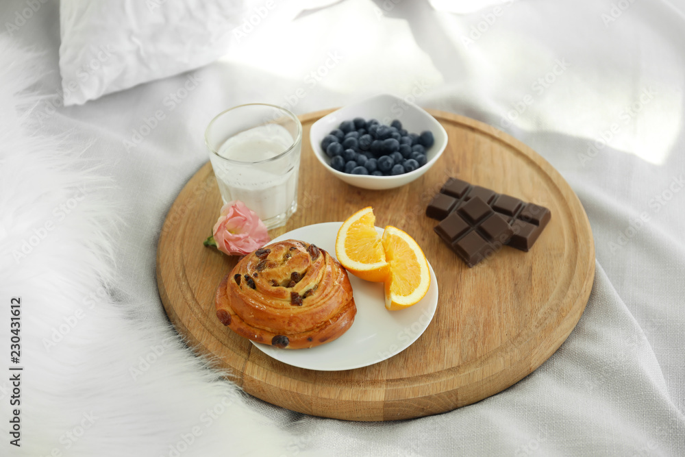 Wooden board with delicious breakfast on bed