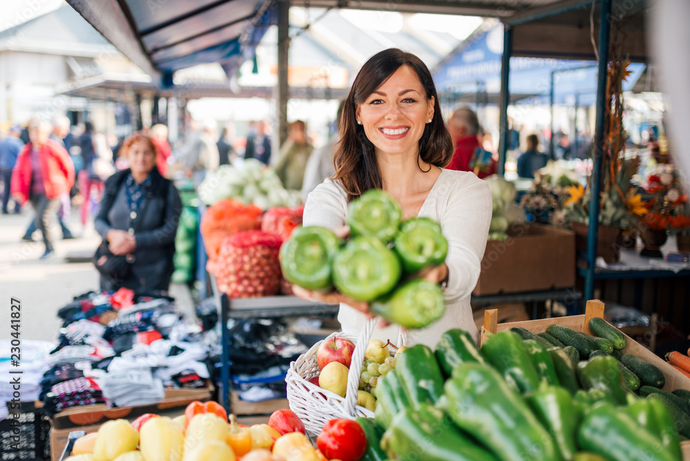 Smiling brunette buying paprika at farmers market.