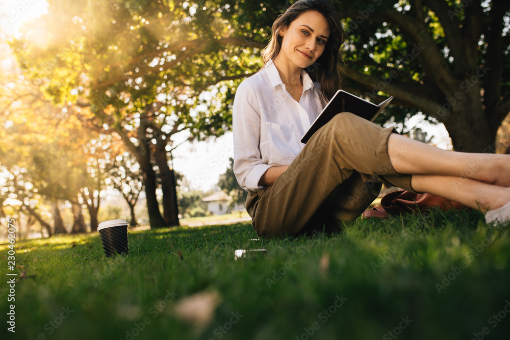 Pretty young woman sitting at park with book