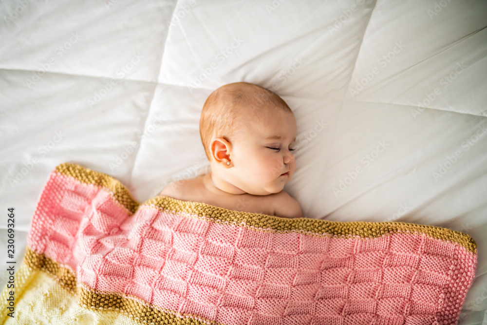 A 4 month baby sleeping on a white bed at home