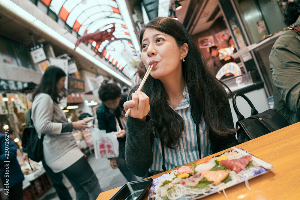 旅行女孩兴奋地吃着新鲜的生鱼