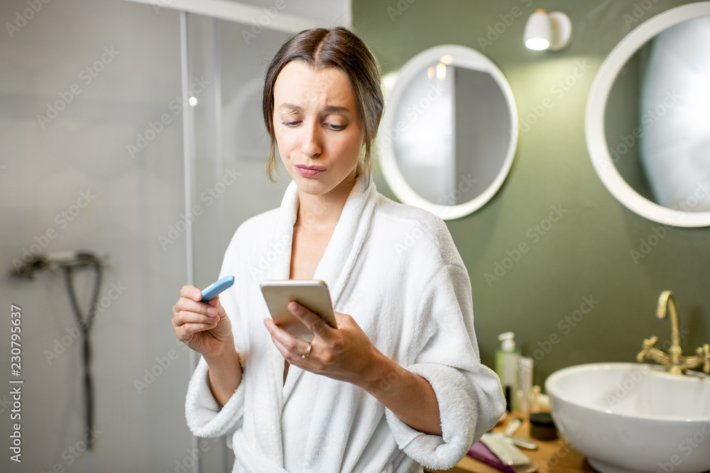 Sad and worried woman in bathrobe waiting for a result looking on a pregnancy test stick in the bath