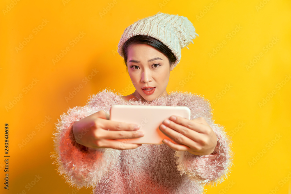 Pretty excited young woman in fur sweater doing taking selfie shot on mobile phone isolated on brigh