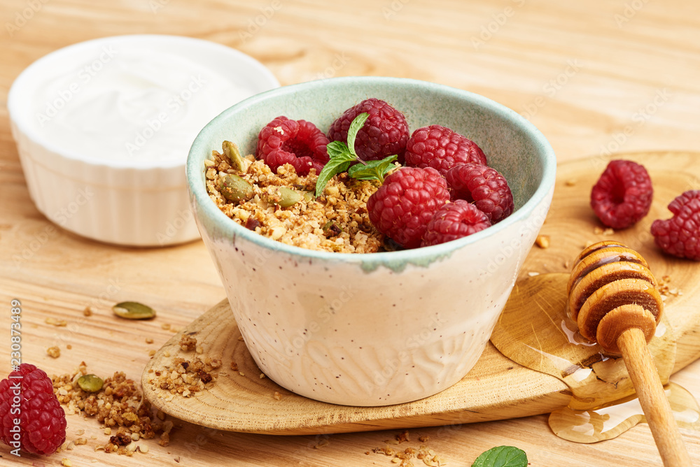 Homemade granola and yogurt in a bowl with raspberries on a wooden table.