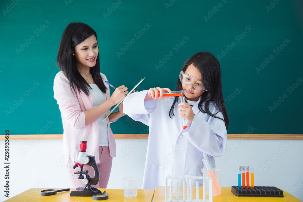 年轻的亚洲女学生在教室里倾倒化学液体，老师站在她旁边。