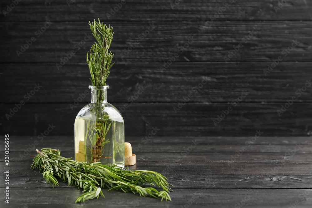 Glass bottle with fresh aromatic rosemary on dark wooden table