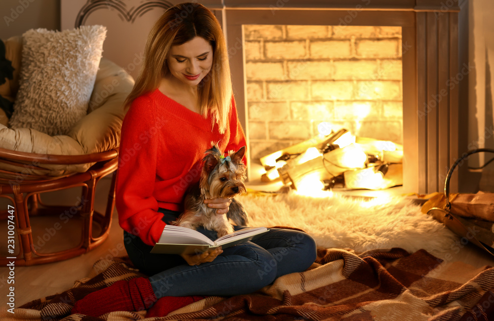 Woman with cute dog reading book near fireplace