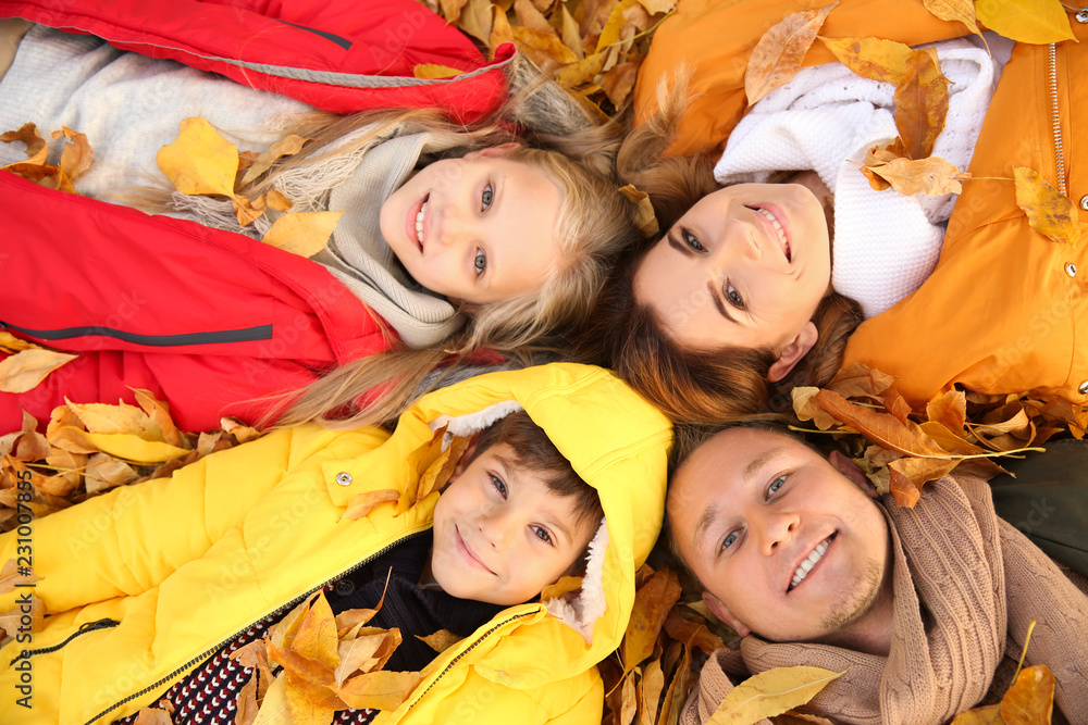 Happy family lying on dry leaves in autumn park