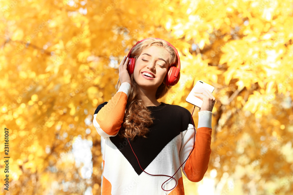 Beautiful young woman listening to music in autumn park