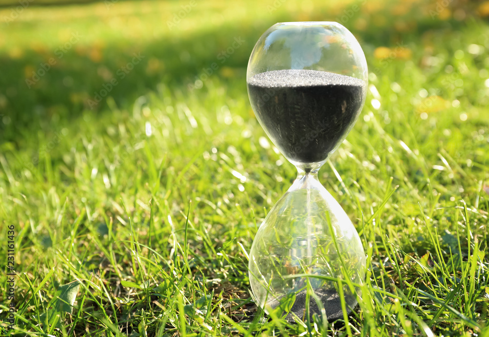 Crystal hourglass with black sand on green grass outdoors