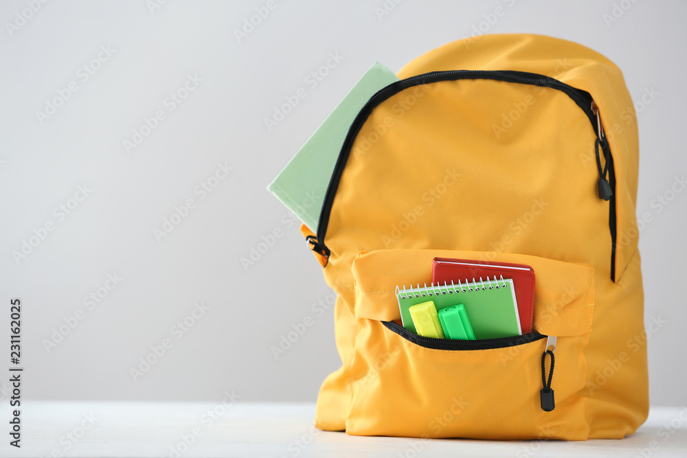 Backpack with school supplies on light background