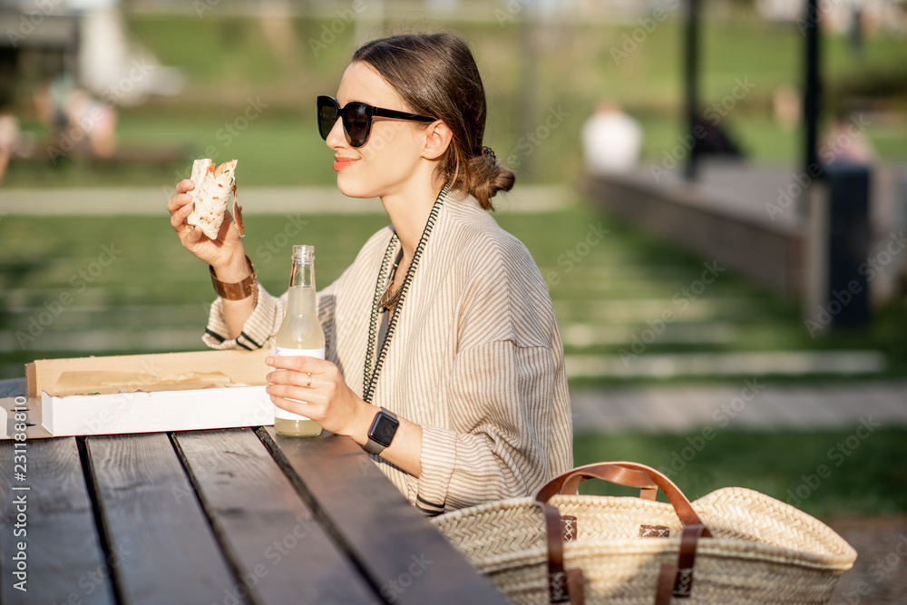 一名年轻女子坐在现代公园的户外吃披萨零食