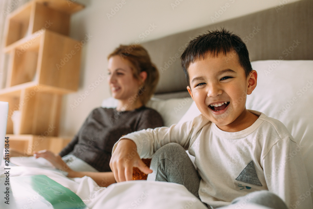 Cute little boy on bed with mother at back