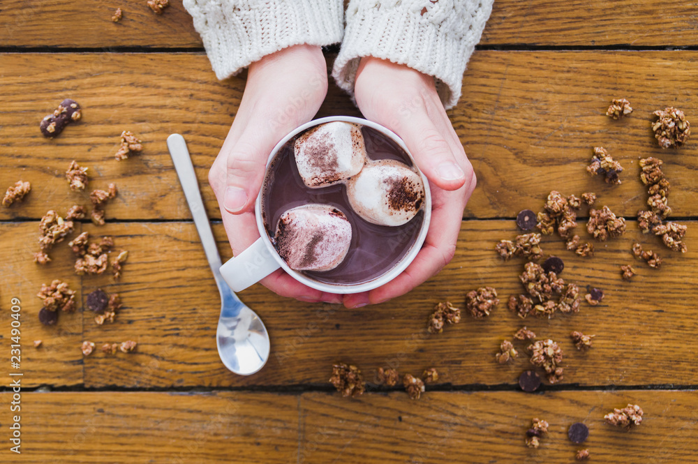 Close up of woman hands holding a hot chocolate cup on a wood table.