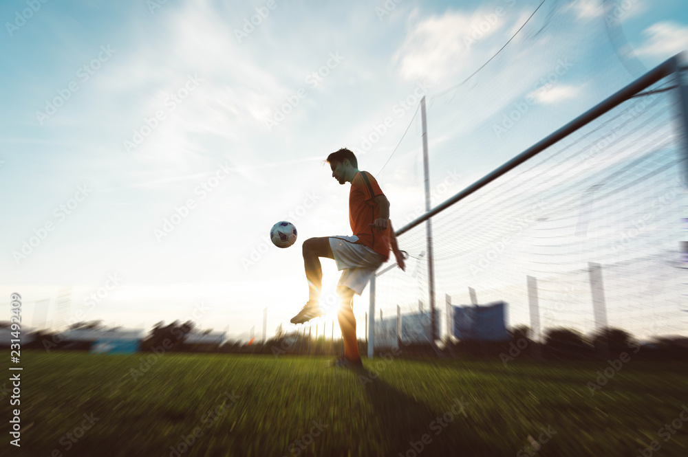 Soccer player is training alone at the stadium at sunset