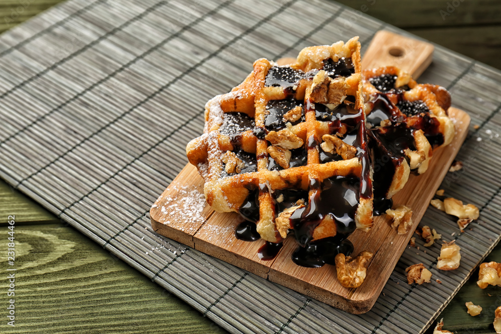 Tasty waffles with chocolate and walnuts on wooden board